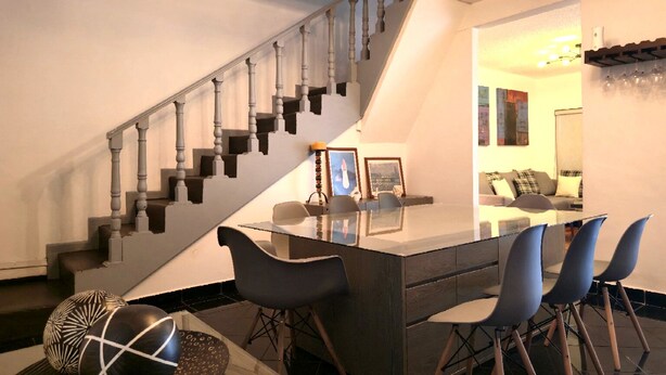 A modern kitchen with a central island, bar stools, a staircase, and a dining area with a sofa and chairs. - Full house in Condesa, 4 bedrooms, terrace and 3 levels (Ciudad de México)