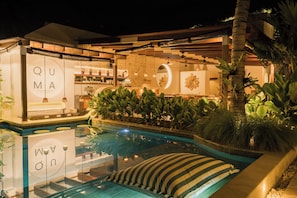 A hotel with a pool, indoor plants, and a sign reading 'QUMA'.