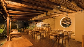 Een restaurant met houten tafels en stoelen, een stenen muur en een ronde spiegel.