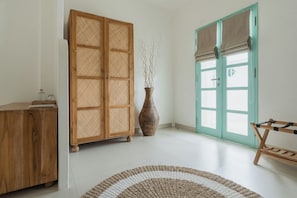 A room with a wooden cabinet, a vase with branches, a bench, and a door with a window.