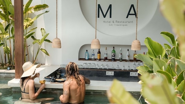 Een zwembadgedeelte met twee personen, een bar met flessen en glazen, en een bord waarop 'Hotel & Restaurant Gili Trawangan' staat.
