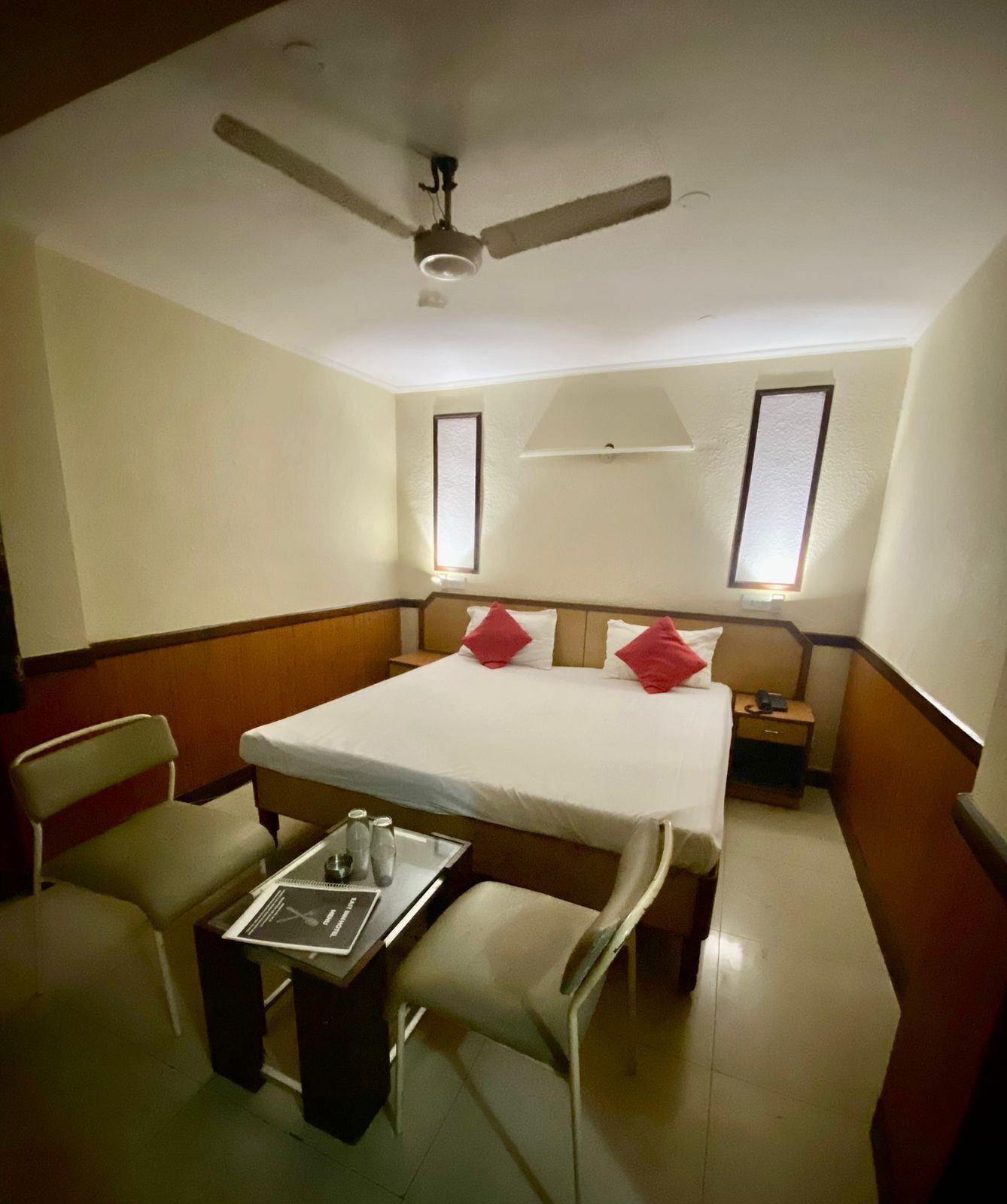 A hotel room with a bed, a desk with a chair, a ceiling fan, and two bedside lamps.