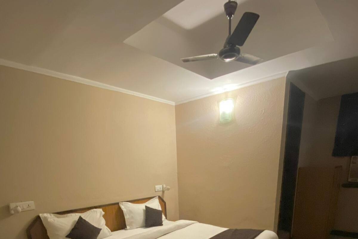 Una cama bien hecha con almohadas y una colcha, una mesita de noche con una lámpara y un ventilador de techo.