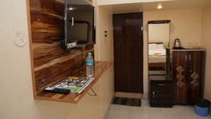 Habitación de hotel con pared de acento de madera, televisor montado, botella de agua, control remoto, cama con almohada, armario y un cubo de basura.