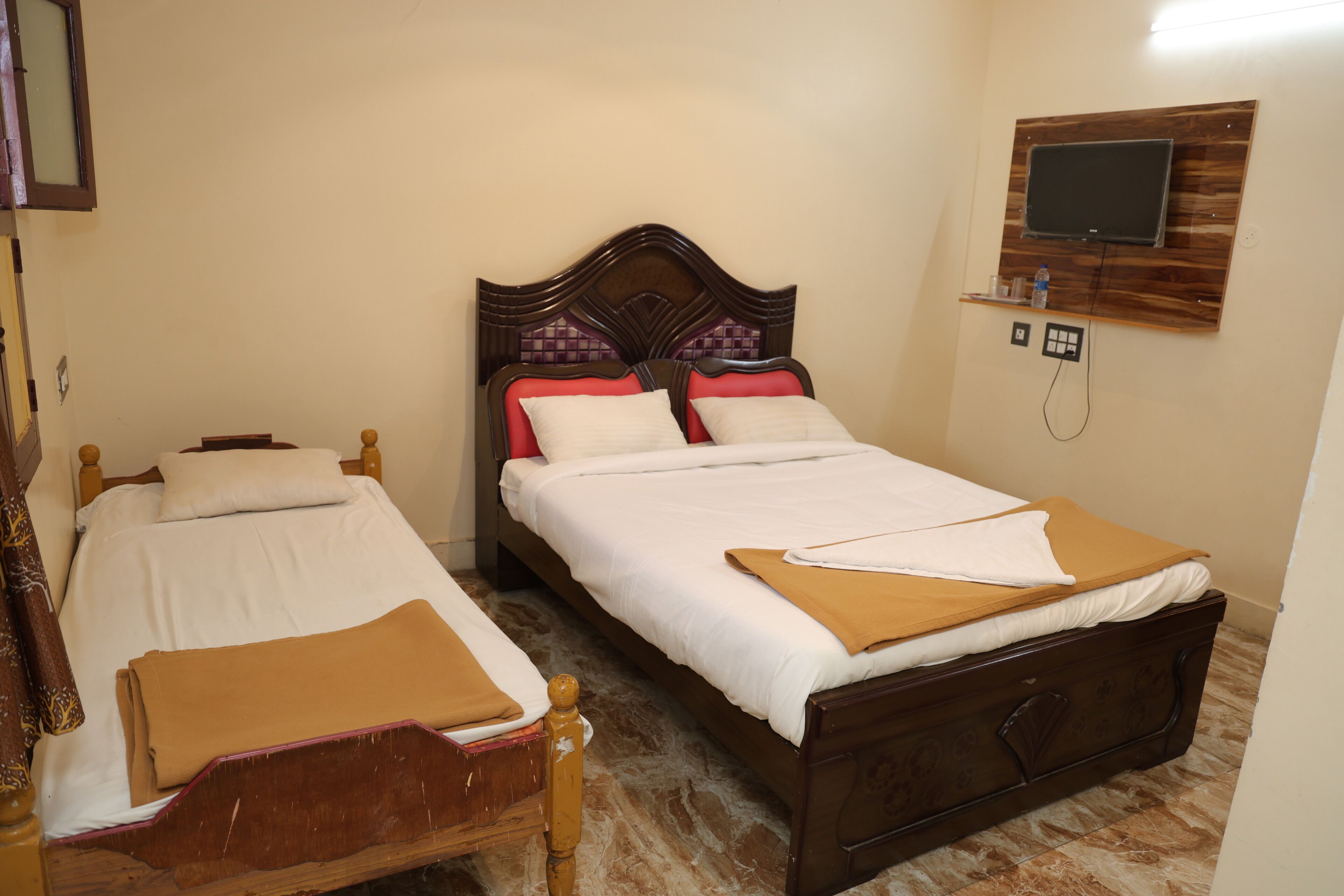 A bedroom with two wooden beds, a TV mounted on the wall, and a power outlet.