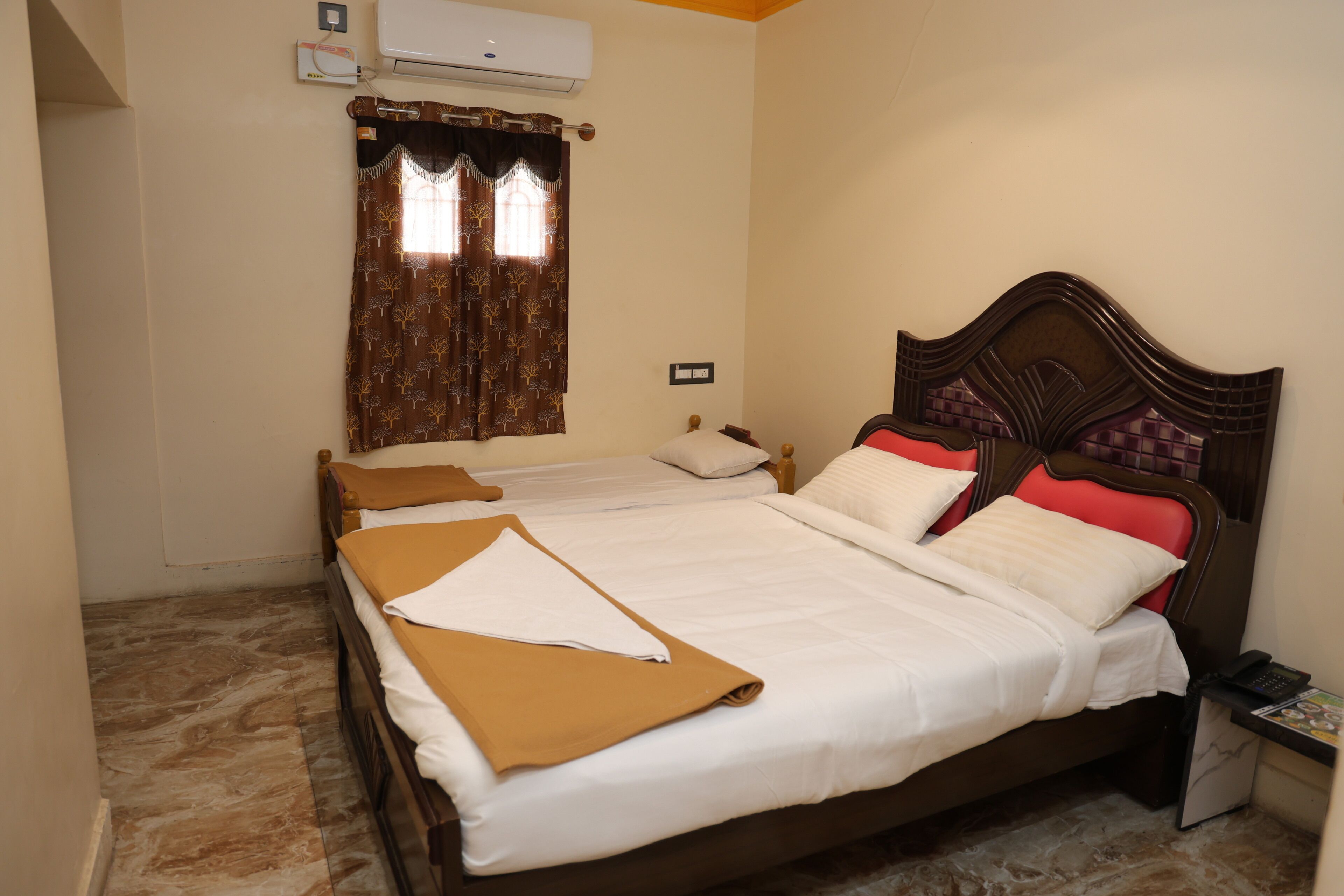 Uma cama de casal com cabeceira de madeira, um criado-mudo com telefone e uma janela com cortinas.