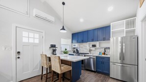 Cozinha moderna com ilha central, armários azuis, eletrodomésticos de aço inoxidável e porta branca.