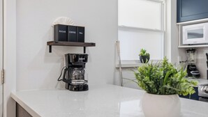 Uma cozinha com cafeteira, prateleira com caixas identificadas, micro-ondas e um vaso de planta.