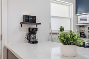 Eine Küche mit Kaffeemaschine, einem Regal mit beschrifteten Boxen, einer Mikrowelle und einem Blumentopf.