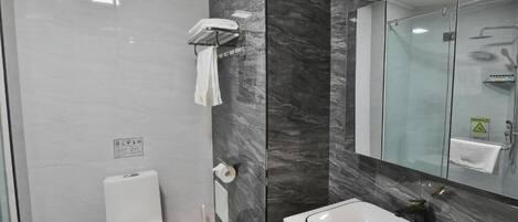 A modern bathroom with a white toilet, a glass shower enclosure, a white sink, and marble walls.