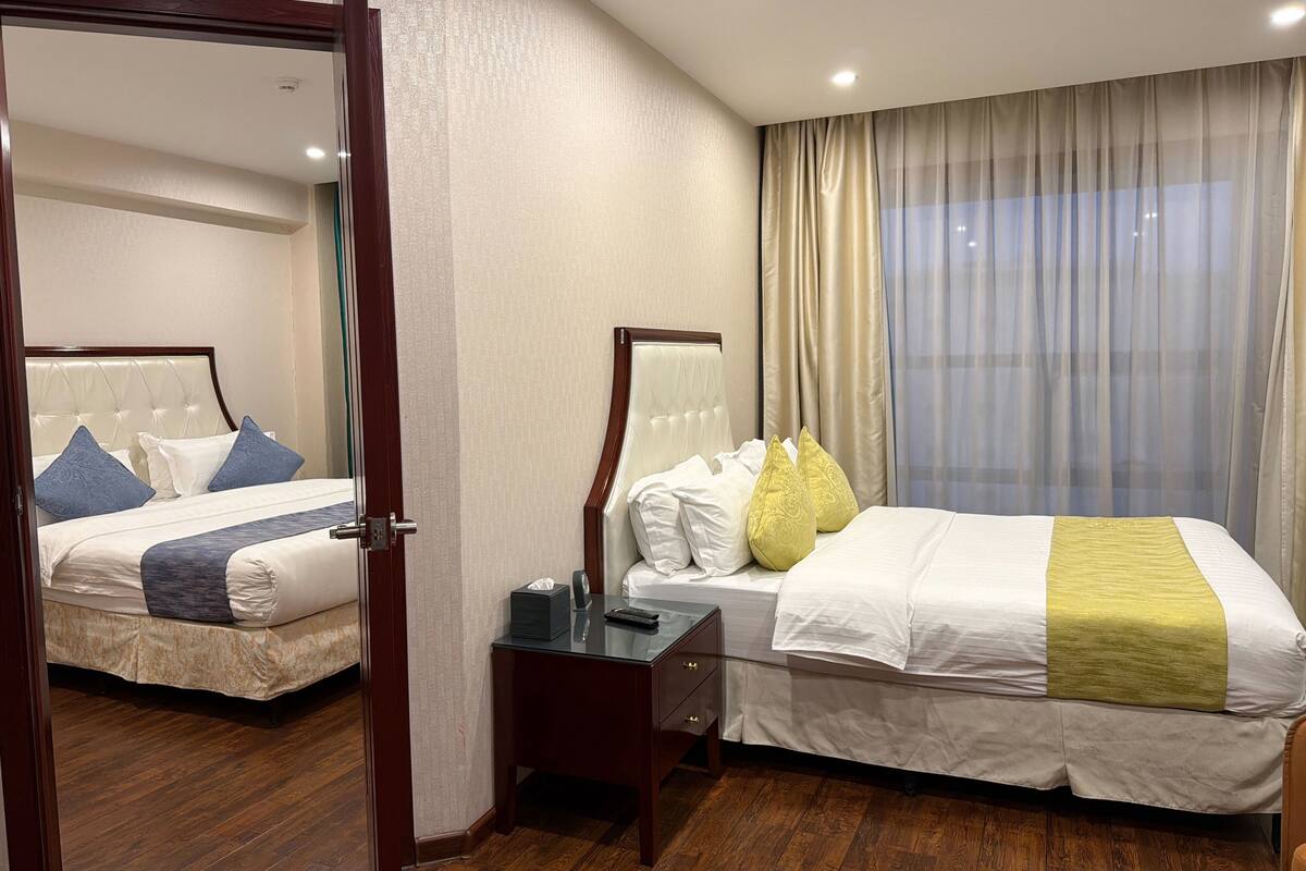 Una habitación de hotel con dos camas, una mesita de noche, un espejo y una ventana con cortinas.