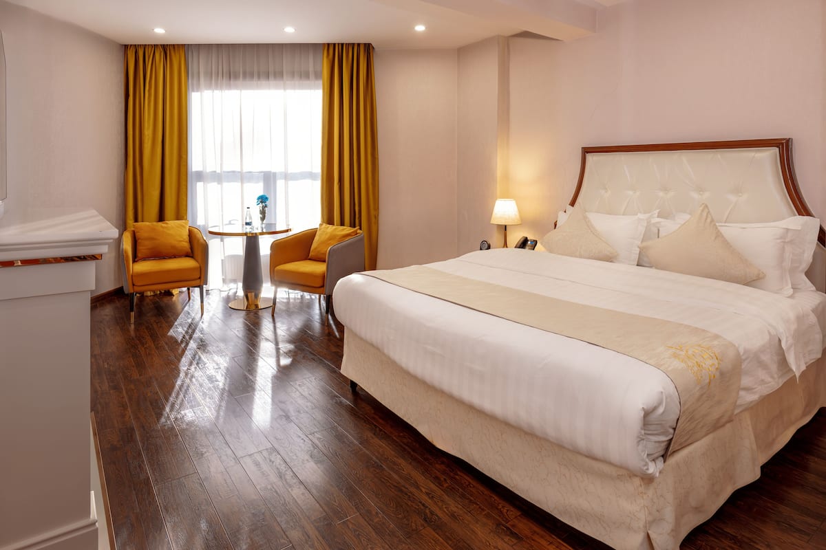 Habitación de hotel con una cama grande, dos sillones, una mesita y un ventanal con cortinas.