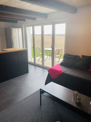 A modern living room with a sofa, a coffee table, a dining table, and a sliding glass door leading to a patio.
