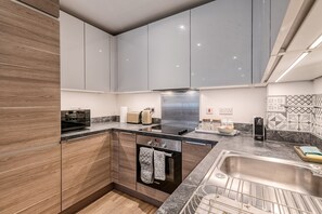 A modern kitchen with a built-in oven, a coffee machine, and a sink. - Modern Surrey Quays Flat (London)