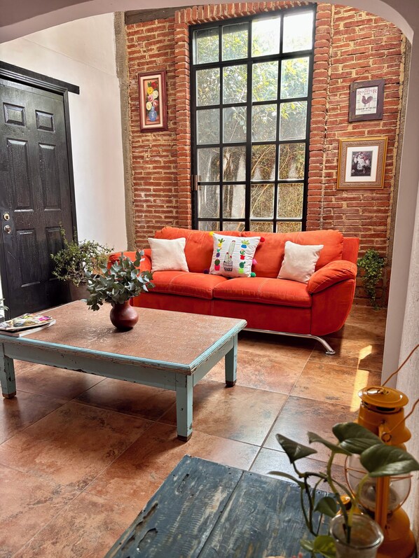 Ein Zimmer mit Backsteinwand, großem Fenster, rotem Sofa, Couchtisch und einer Tür.