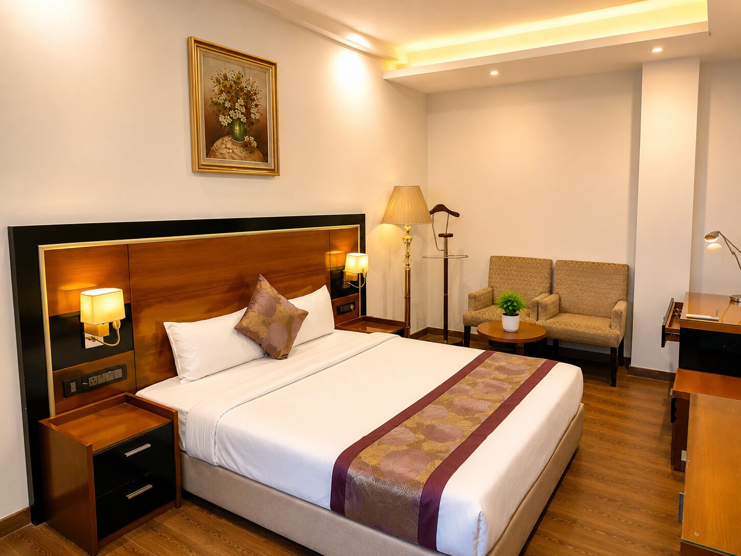 Una habitación de hotel con una cama, mesitas de noche, una lámpara, una silla y un escritorio.