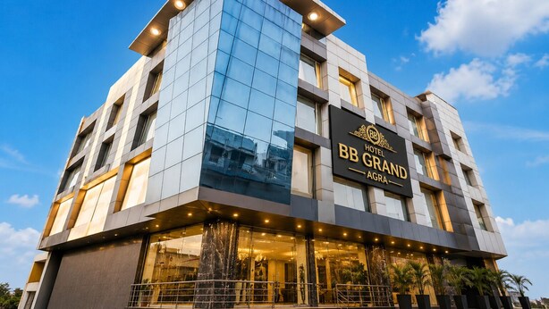 A modern hotel building with a reflective glass facade, a prominent sign for 'BB GRAND,' and a visible entrance with a metal railing. - Hotel BB Grand Agra (Agra)