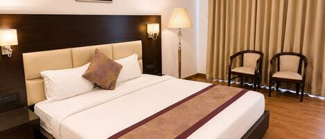 A hotel room with a large bed, two bedside lamps, a painting on the wall, and two chairs by the window.