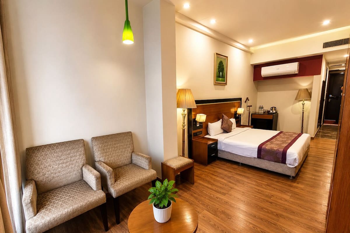 Quarto de hotel com uma cama, duas poltronas, uma pequena mesa com uma planta, mesa de cabeceira, abajur e um quadro na parede.