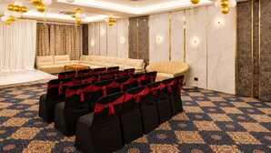 A conference room with a stage, a sofa, and rows of chairs with red sashes. - Hotel BB Grand Agra (Agra)