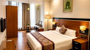 A hotel room with a large bed, bedside tables, a desk, a chair, a TV, and a painting on the wall. - Hotel BB Grand Agra (Agra)