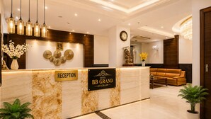 A hotel reception area with a marble counter, a reception desk, a clock, a chandelier, and a sofa. - Hotel BB Grand Agra (Agra)
