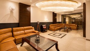 A modern lobby with leather sofas, a glass coffee table, and a large chandelier. - Hotel BB Grand Agra (Agra)