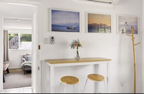 Una habitación con pared blanca, una mesa de madera con dos taburetes y tres cuadros con paisajes.