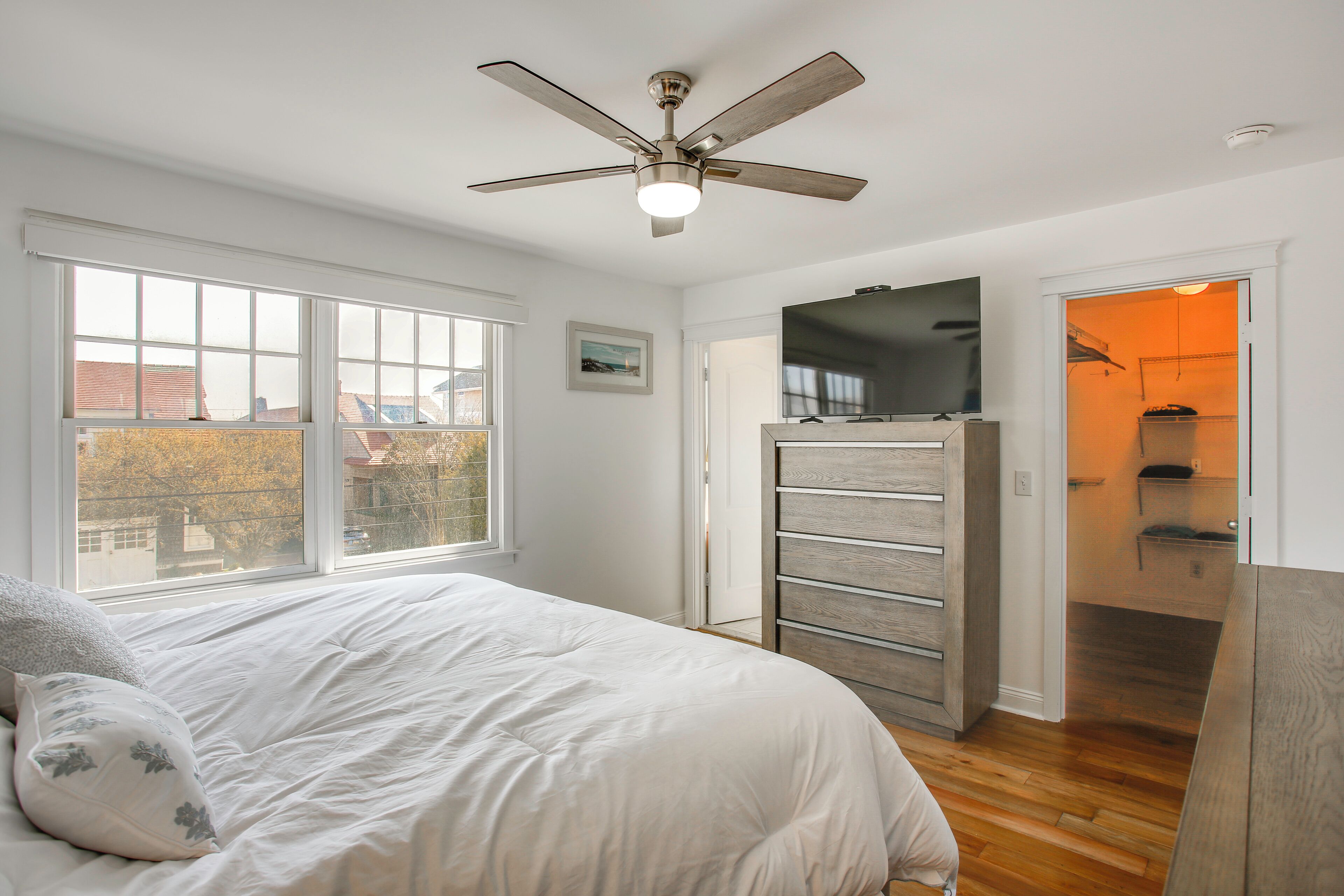 Un dormitorio con cama, ventilador de techo, televisor y vista al exterior.