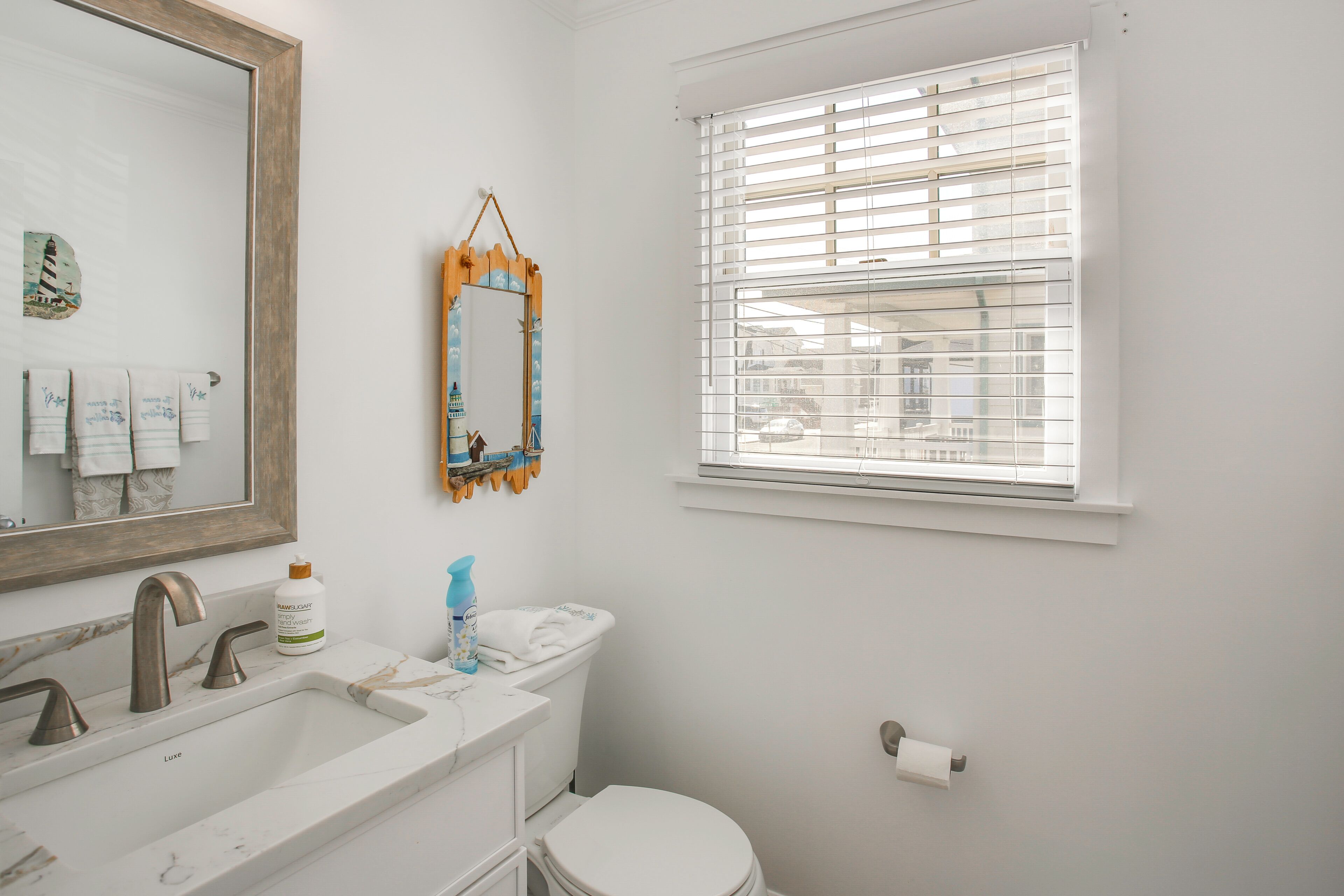 Une salle de bain avec un lavabo, un miroir, des toilettes et une fenêtre.