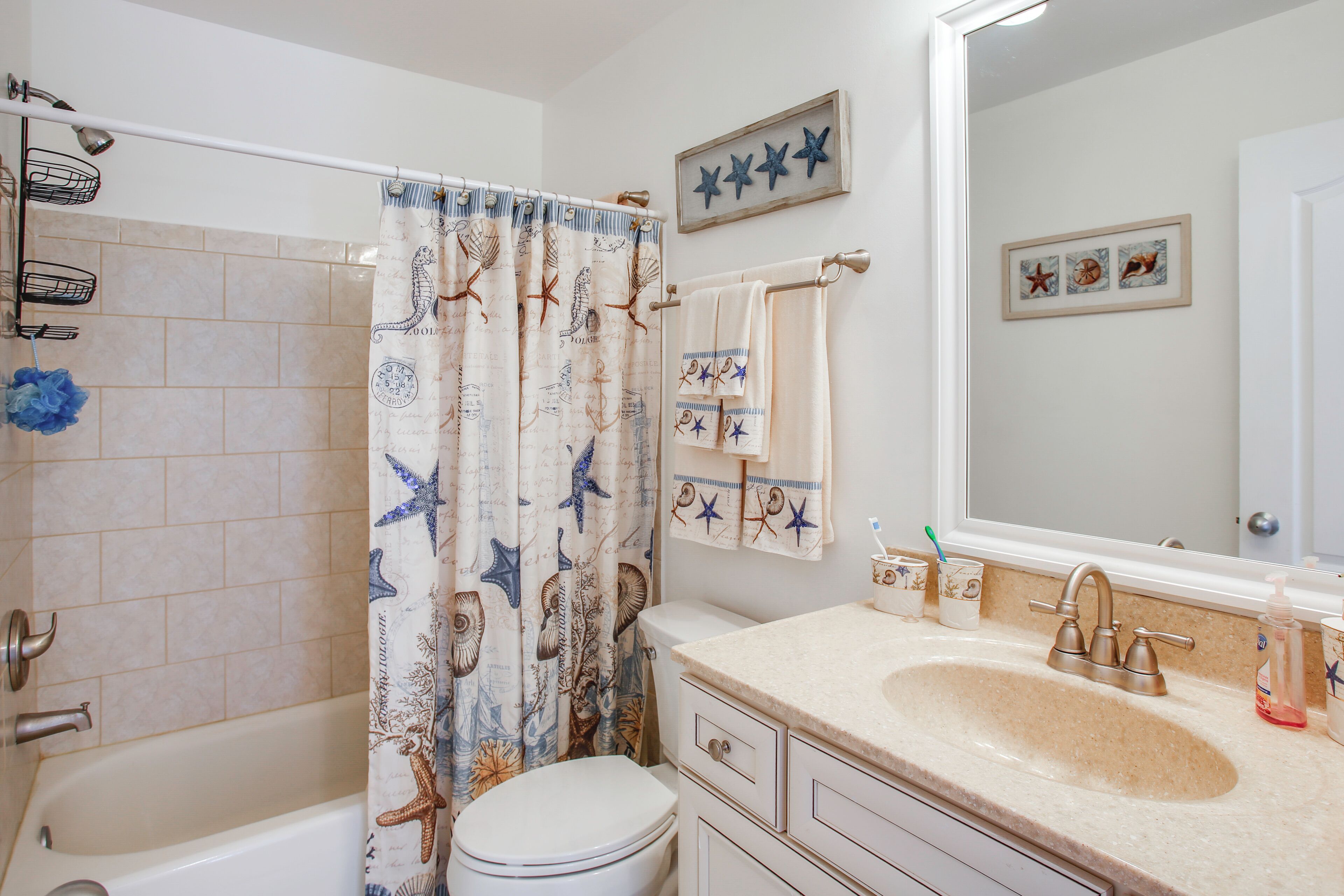 Un baño con bañera, inodoro, lavabo y cortina de ducha con estrellas de mar y conchas marinas.