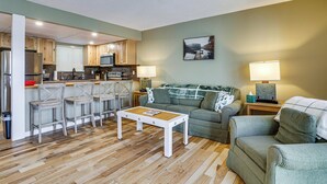 Un salon comprenant un canapé, une table basse et un coin cuisine avec des meubles en bois et un réfrigérateur.