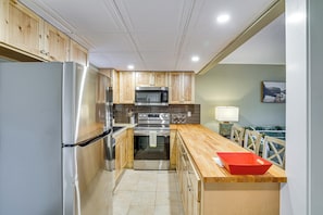 A modern kitchen with wooden cabinets, stainless steel appliances, and a wooden countertop.