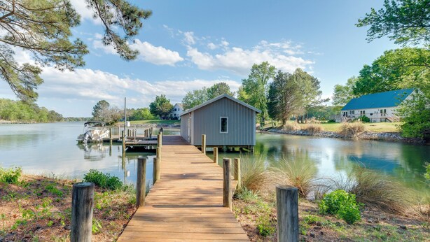 A wooden dock leading to a small shed by a calm lake, surrounded by trees and a house with a blue roof. - Dock Access! Family Retreat on the Little Wicomico (Heathsville)