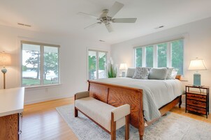 Quarto com cama, um banquinho, mesa de cabeceira e ventoinha no teto.