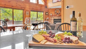 L’intérieur d’un chalet en bois présente une table à manger dressée pour une dégustation de fromages et de vins, avec une variété de fromages, de charcuteries et de raisins.