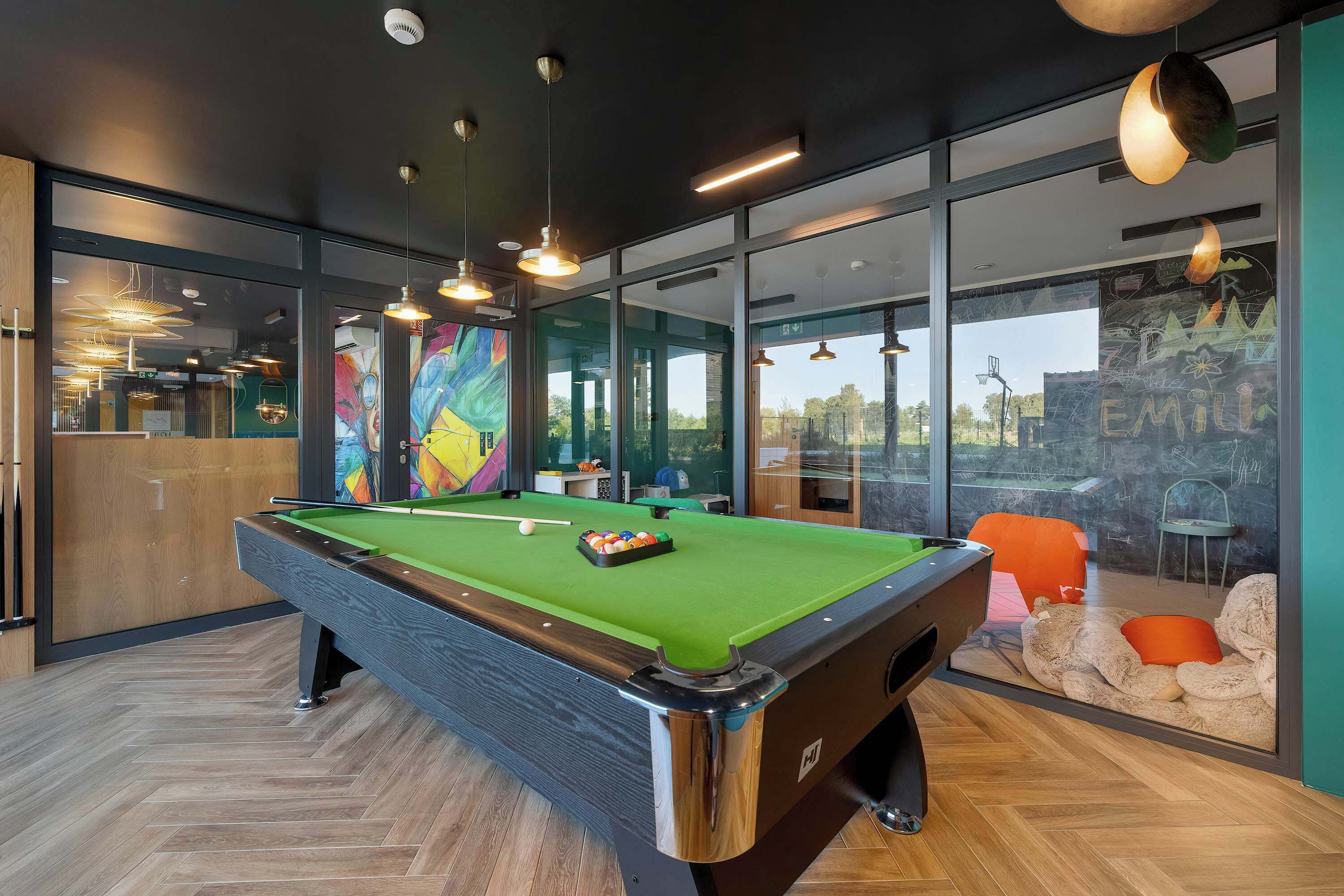 Una mesa de billar en una habitación moderna con ventanas amplias, suelo de madera e iluminación colgante.