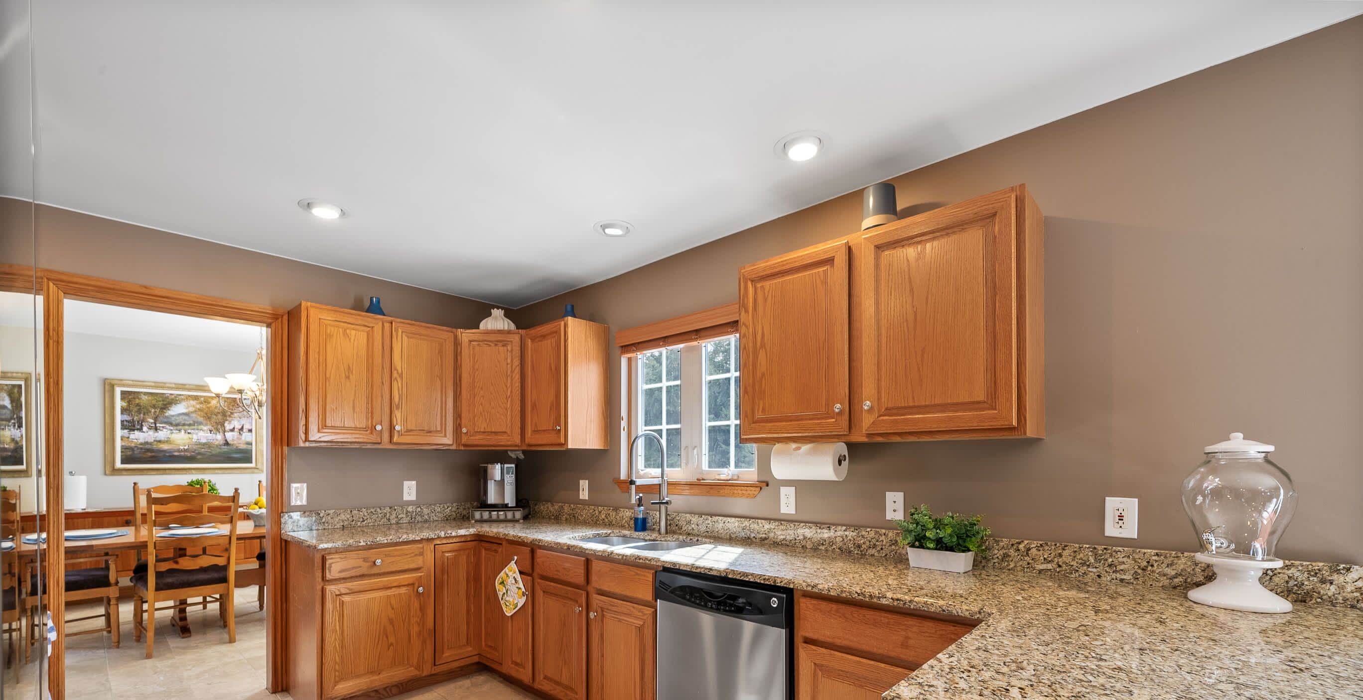 A kitchen with wooden cabinets, granite countertops, a dishwasher, and a window.