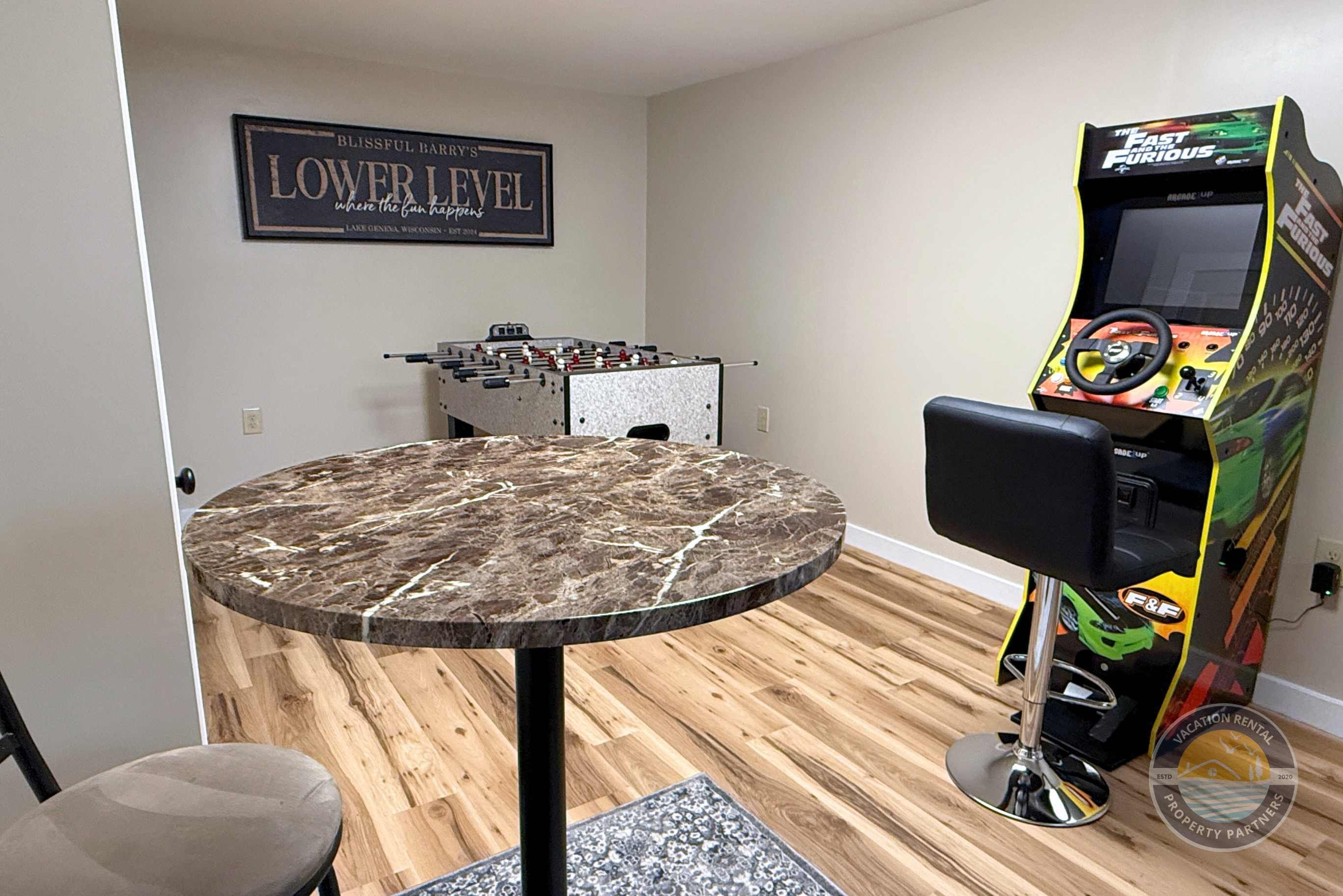 Une pièce équipée d’un baby-foot, d’une console de jeux, d’une table ronde avec un plateau en marbre et d’un panneau affiché au mur.