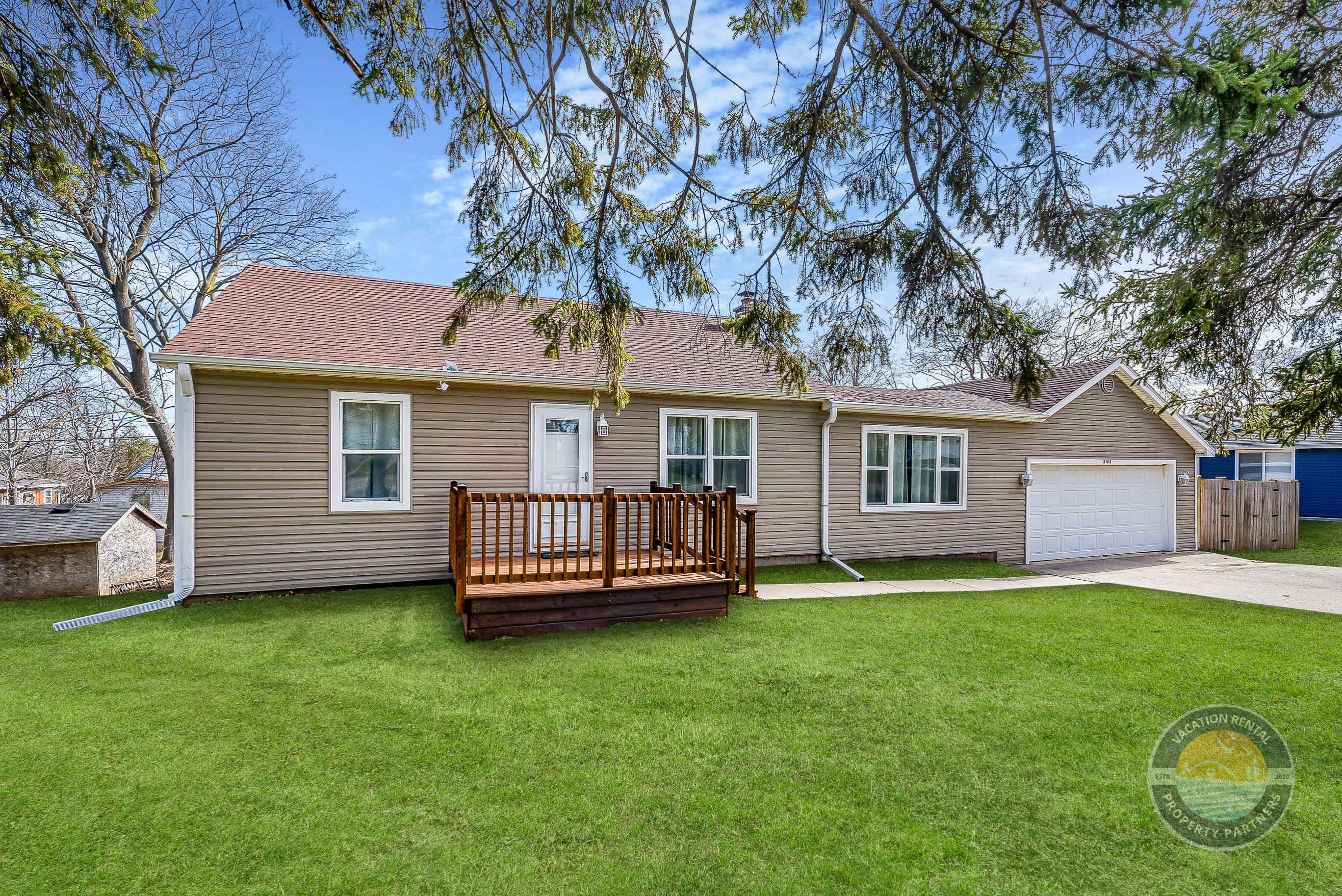 A single-story house with a front deck, a garage, and a well-maintained lawn.