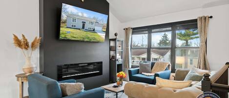 Una sala de estar moderna con televisor montado, asientos cómodos, chimenea y un ventanal con cortinas.