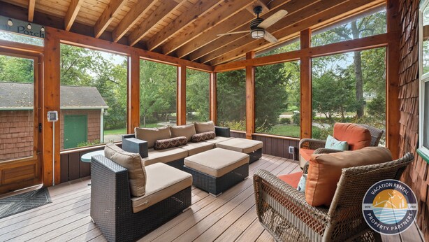A covered outdoor deck with wooden beams, large windows, and wicker furniture. - Lake Geneva Escape 4BR Arcade Fire Pit and Deck (Lake Geneva)