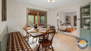 A dining area with a wooden table set for four, a bench, and a view of the outdoors through large windows. - Lake Geneva Escape 4BR Arcade Fire Pit and Deck (Lake Geneva)