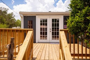 A wooden deck leading to a building with a white door and windows, surrounded by greenery. - Firefly Lakehouse 3 br, 2 Bath, pet Friendly (Canyon Lake)
