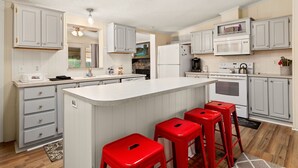 Una cocina moderna con armarios blancos, una isla grande con taburetes rojos, un microondas y un refrigerador.