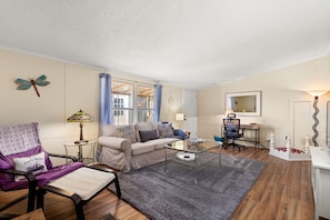 A living room with a sofa, armchair, coffee table, lamp, and a desk with chair. - Firefly Lakehouse 3 br, 2 Bath, pet Friendly (Canyon Lake)