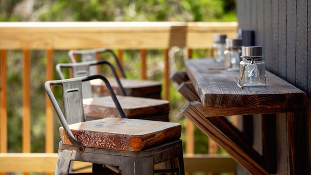 Una terraza de madera con sillas metálicas y una mesa, con botellas sobre la mesa.