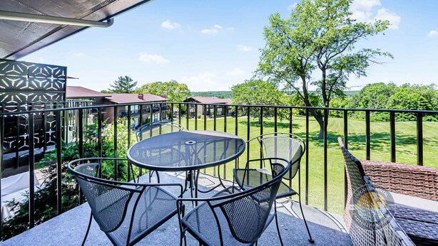 A balcony with a table and chairs, a view of a green lawn, and a building in the background. - Modern Lake Geneva Condo With Pool and Patio (Lake Geneva)