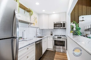 A modern kitchen with white cabinetry, stainless steel appliances, and a herringbone tile backsplash.