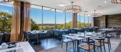 A modern restaurant with high ceilings, large windows, and elegant chandeliers.